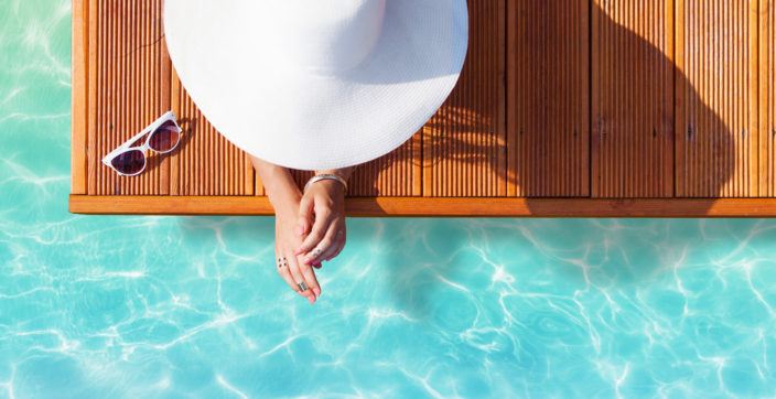 Summer holiday fashion concept - tanning woman wearing sun hat on a wooden pier view from above