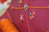 close-up photography of orange sewing thread near red leather cushion