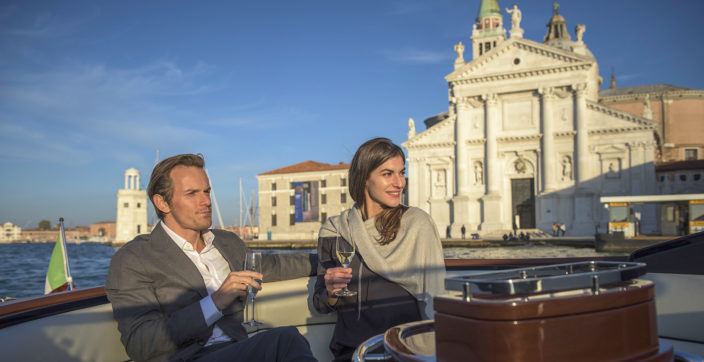 man and woman sitting on boat deck while holding wine glasses at daytime
