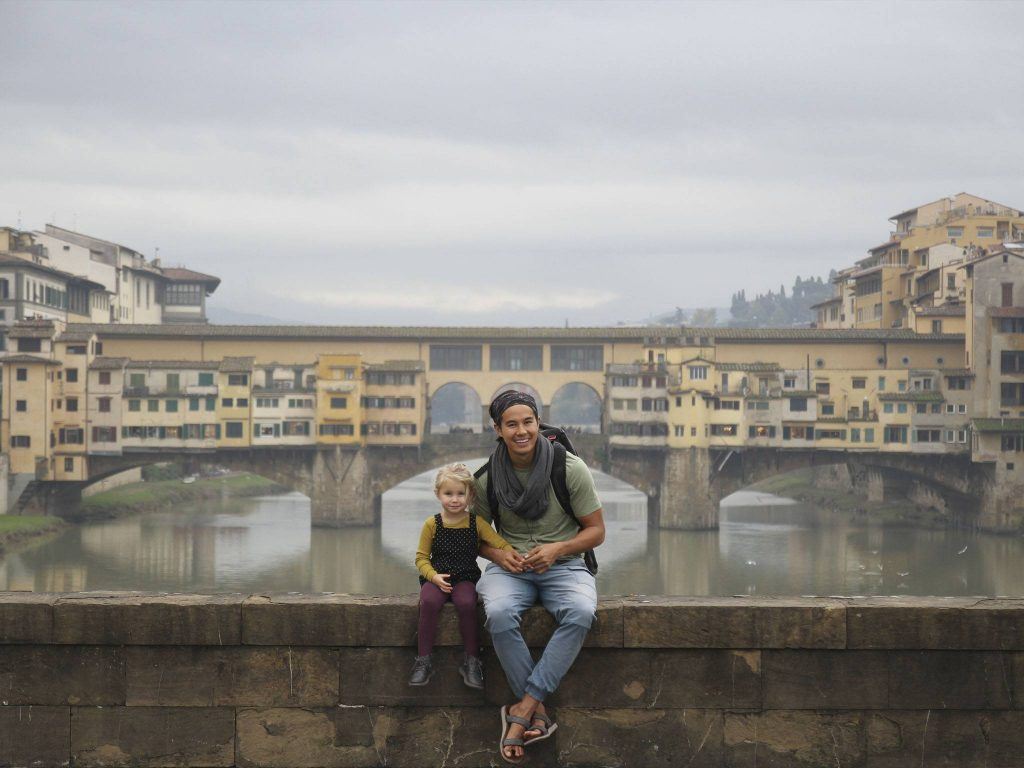 man and girl sitting on concrete bench in front of bridge at daytime