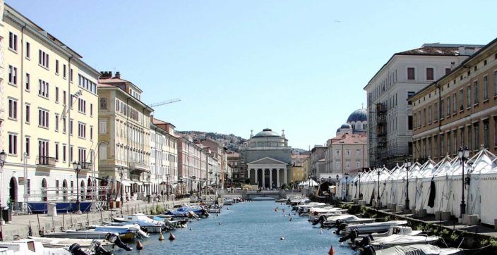 an Italian canal in Trieste lined with boats with a grand religious building at the end of it