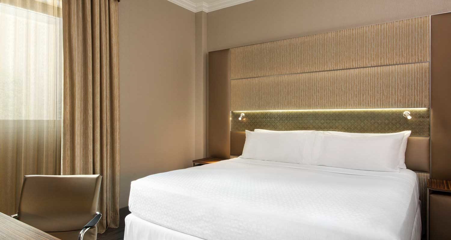 A king-size bed in a hotel suite with a white linens and a gold-colored headboard