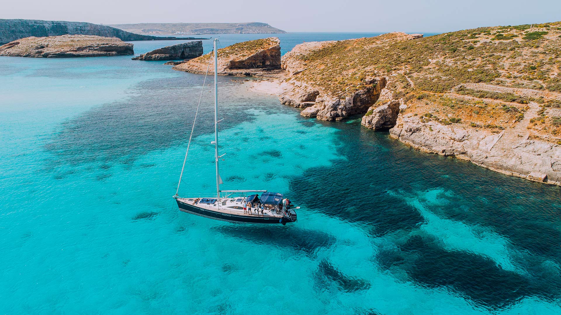 Aerial of Yacht in a crystal clear Blue Lagoon, off Comino