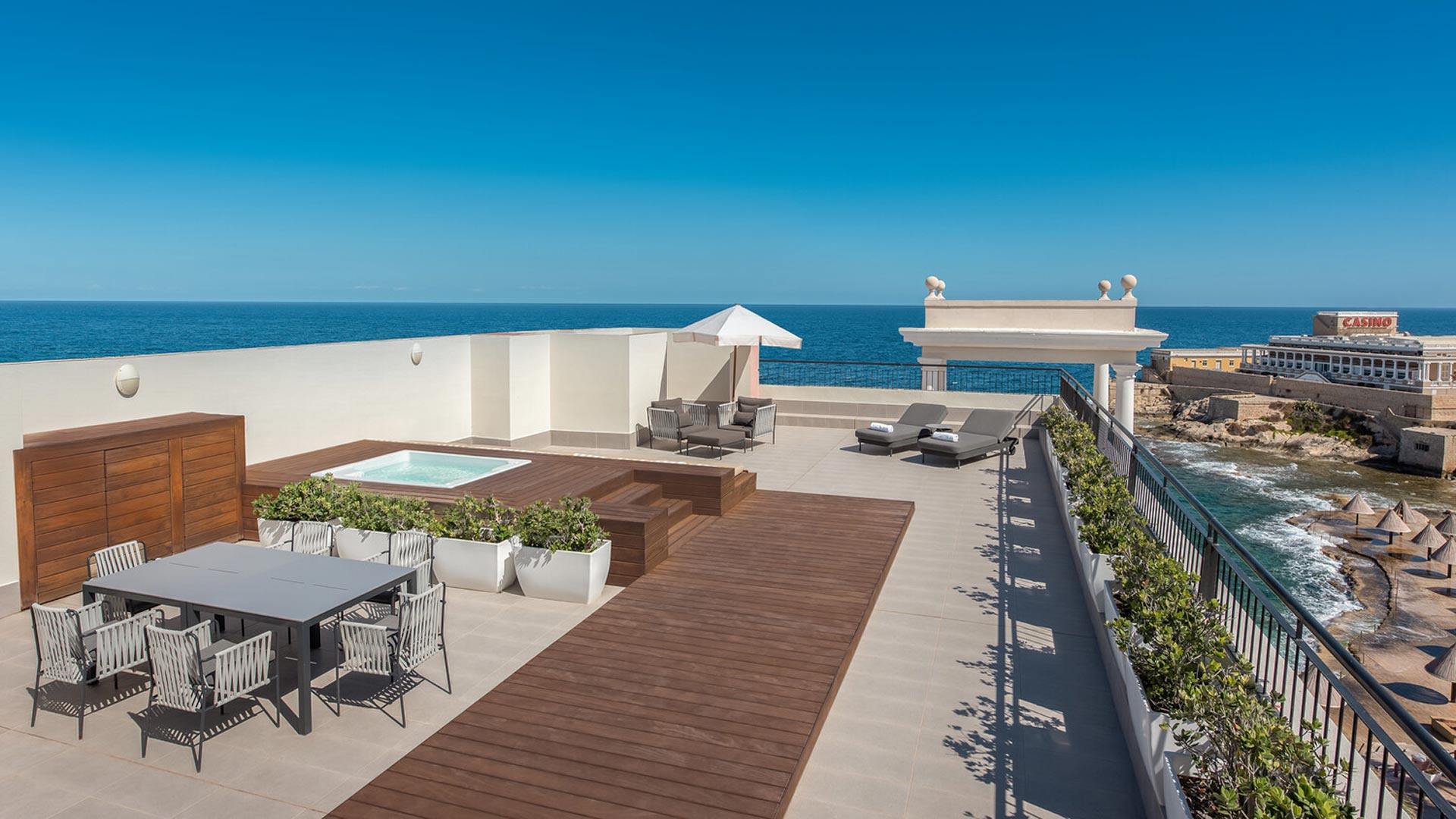 large private terrace outside of a luxury ocean-side suite with a wooden walk-way to a hot tub and an outdoor table and chairs set